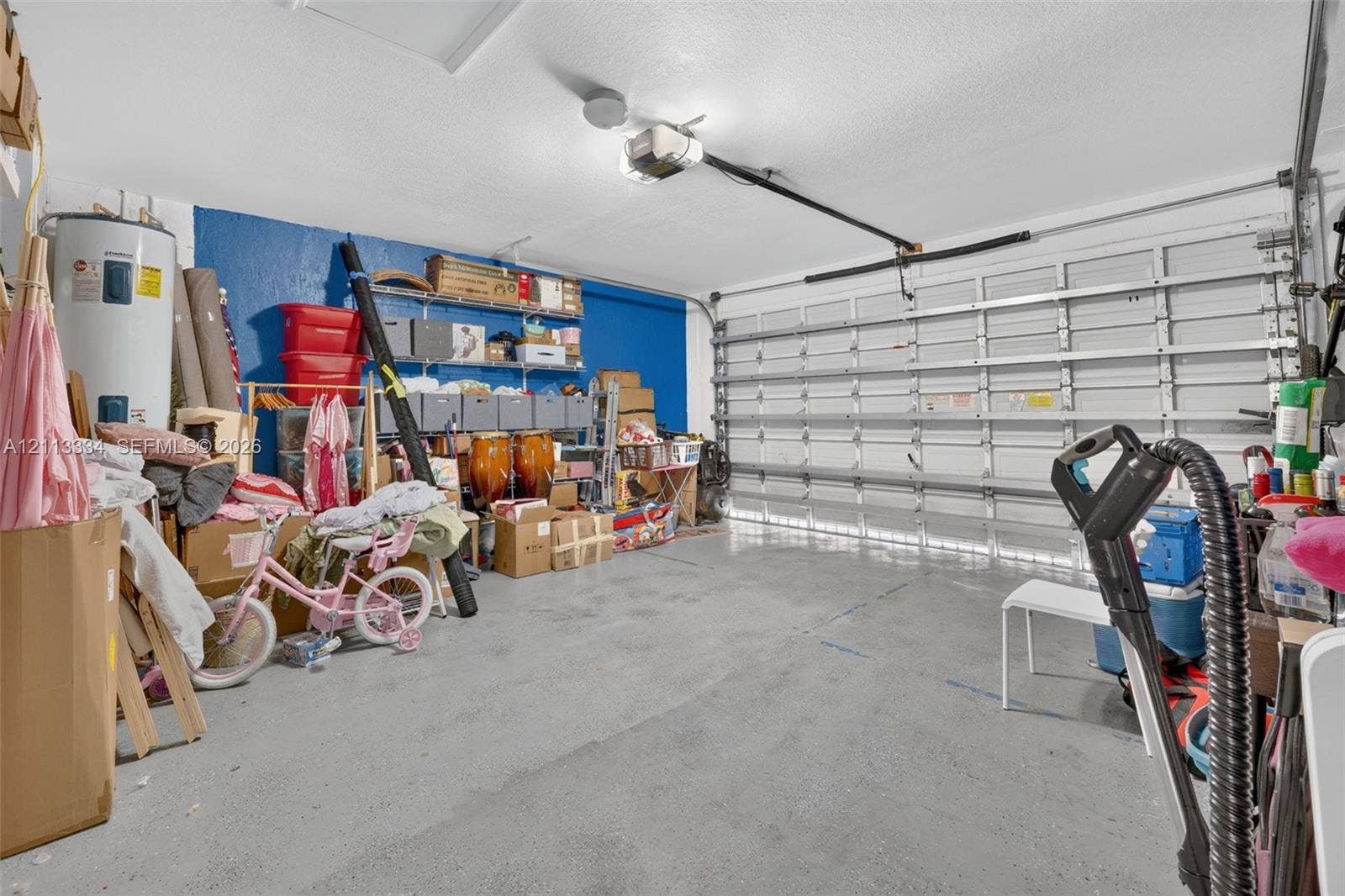 28232 SW 128th Path, Homestead, FL 33033 Two-car garage featuring a sectional overhead door, automated door opener, wall-mounted storage shelving, and a water heater