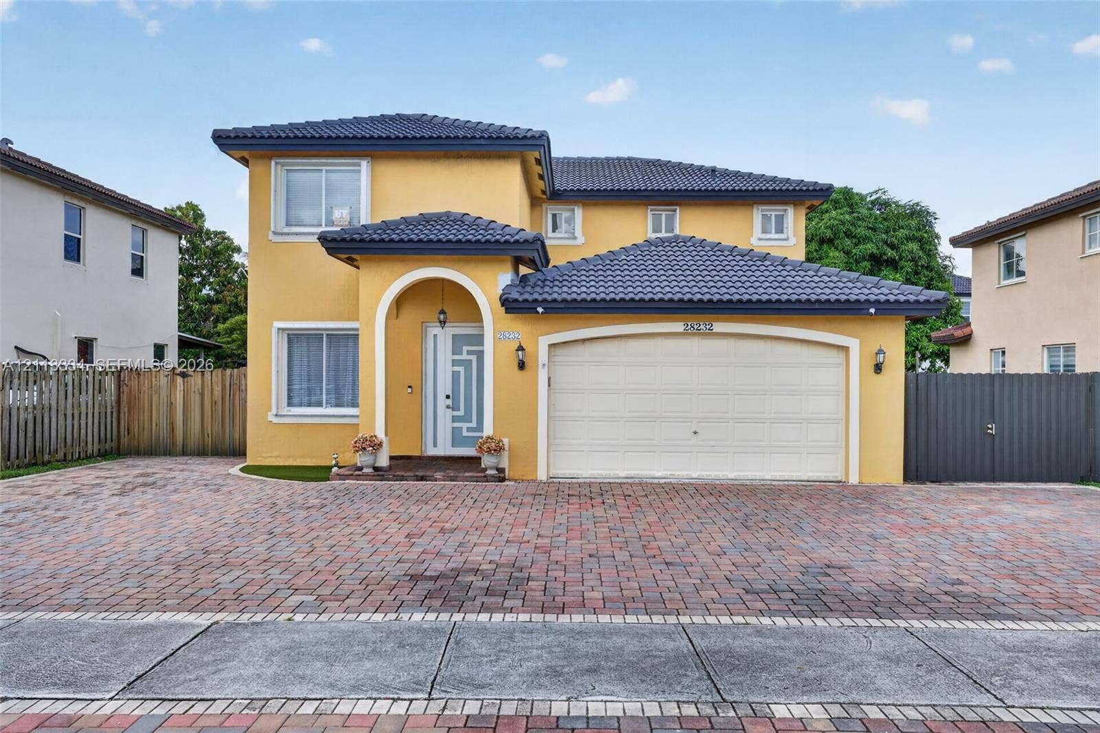 28232 SW 128th Path, Homestead, FL 33033 Two-story exterior featuring a tile roof, an arched entry, a geometric glass-panel front door, and a multi-car brick paver driveway