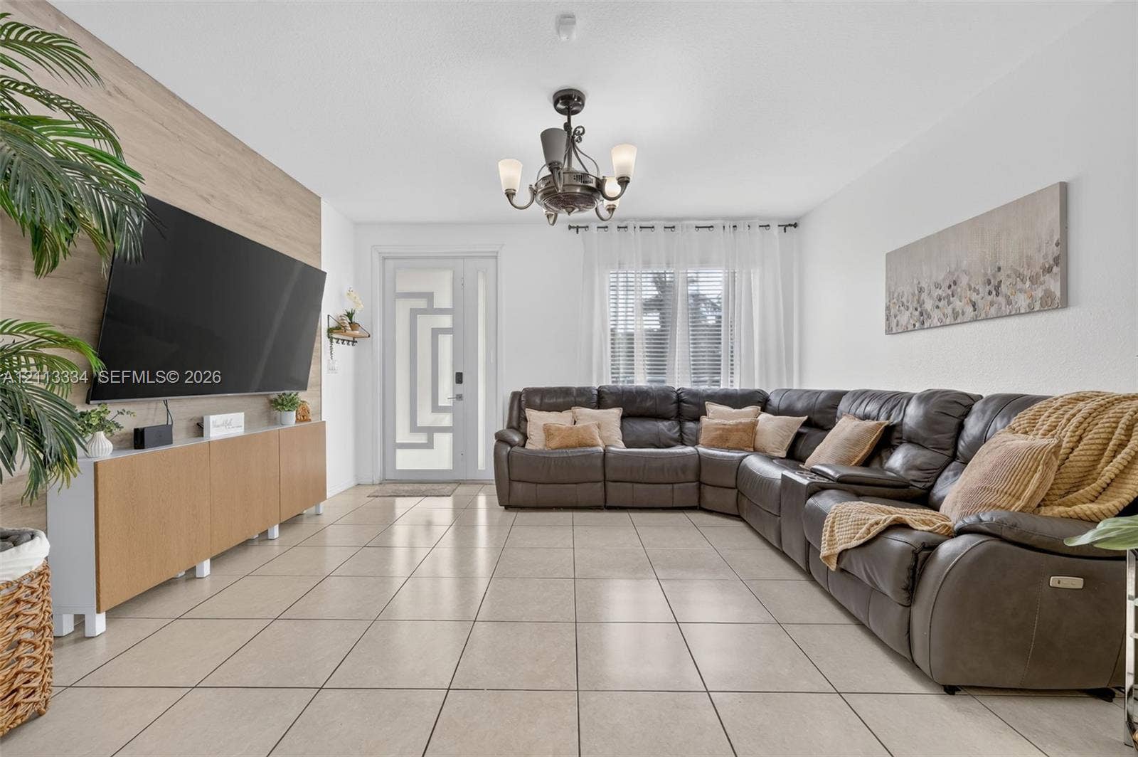 28232 SW 128th Path, Homestead, FL 33033 Living area featuring large-format tile flooring, a geometric paneled entry door, a floor-to-ceiling wood-finish accent wall, and a multi-arm chandelier