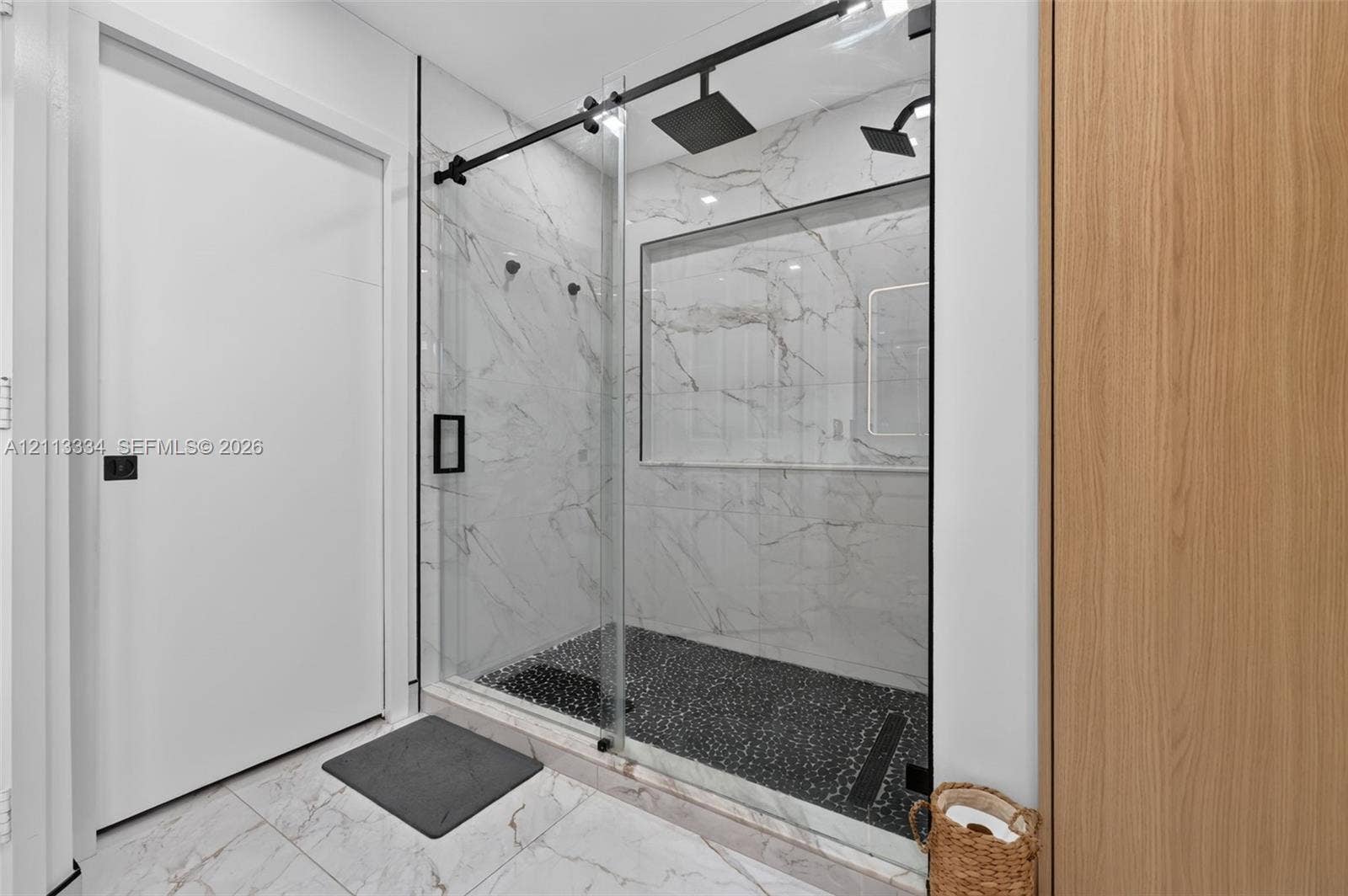 28232 SW 128th Path, Homestead, FL 33033 Walk-in shower featuring large-format wall tiling, a sliding glass door, matte black hardware, a rainfall showerhead, and a recessed wall niche