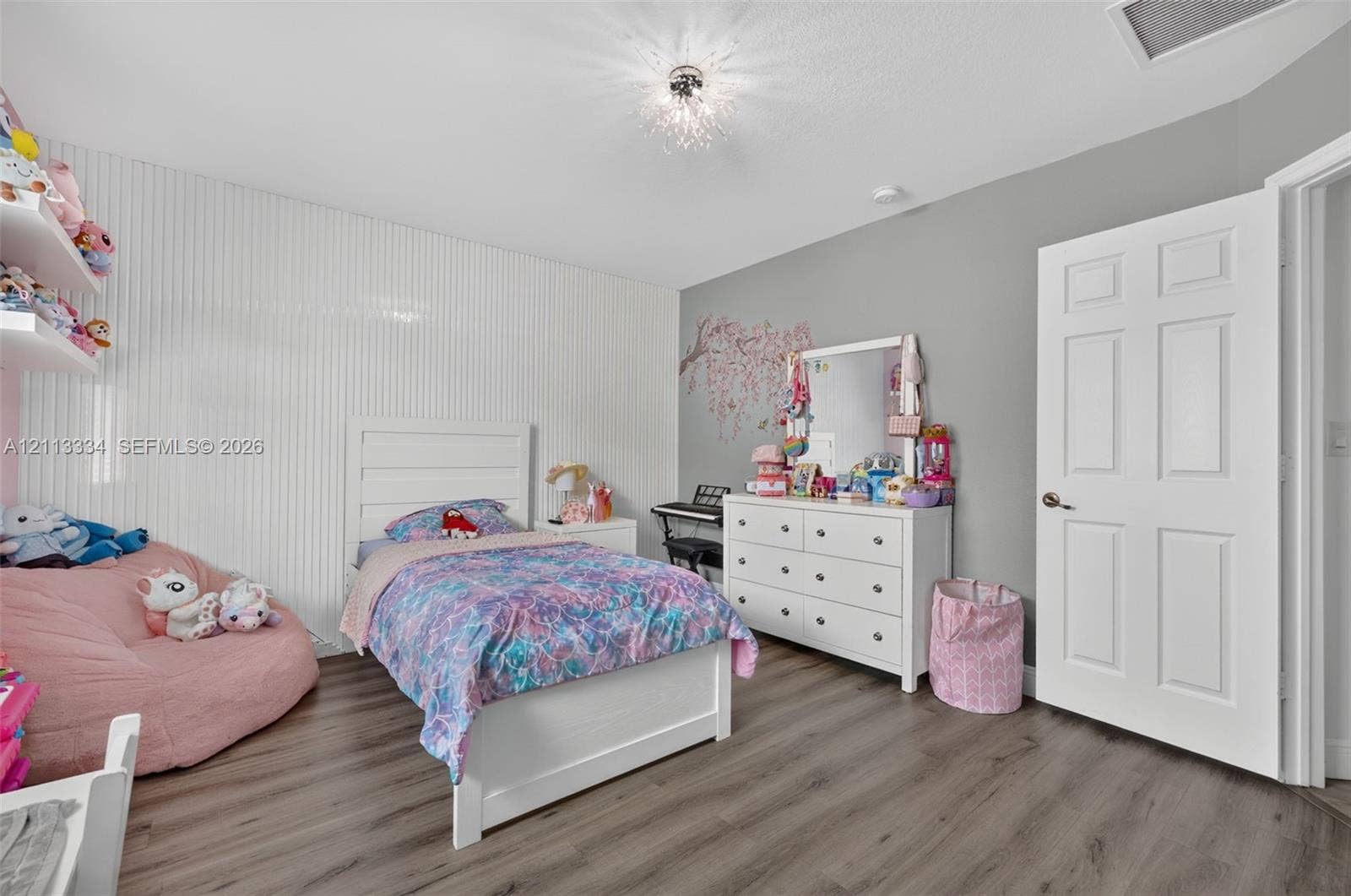 28232 SW 128th Path, Homestead, FL 33033 Bedroom featuring wood-finish flooring, textured vertical wall paneling, a six-panel interior door, and a decorative flush-mount ceiling fixture