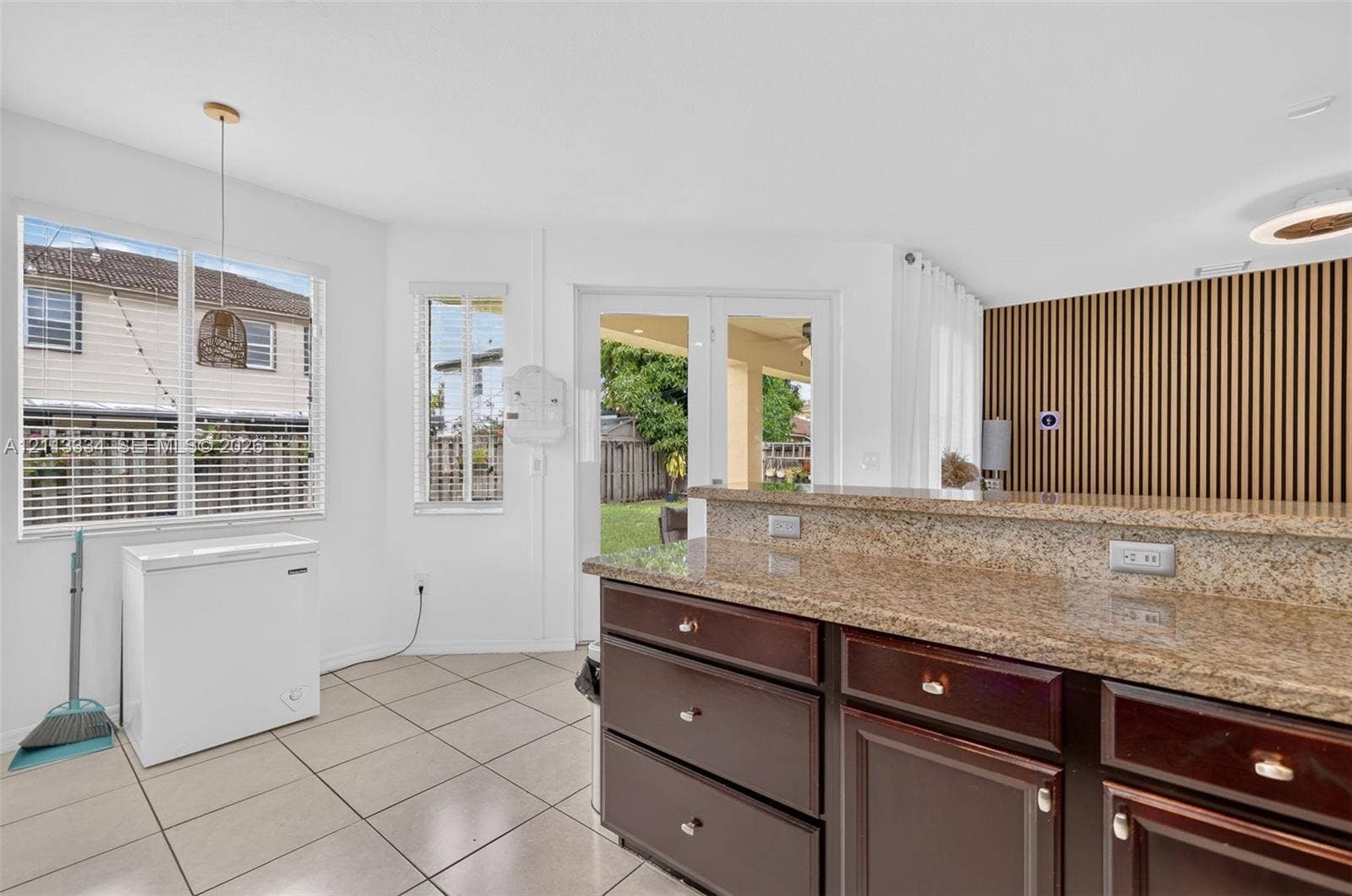 28232 SW 128th Path, Homestead, FL 33033 Kitchen featuring dark-toned cabinetry, stone-finish countertops, tile flooring, decorative vertical wood-slat wall paneling, and glass-paneled doors