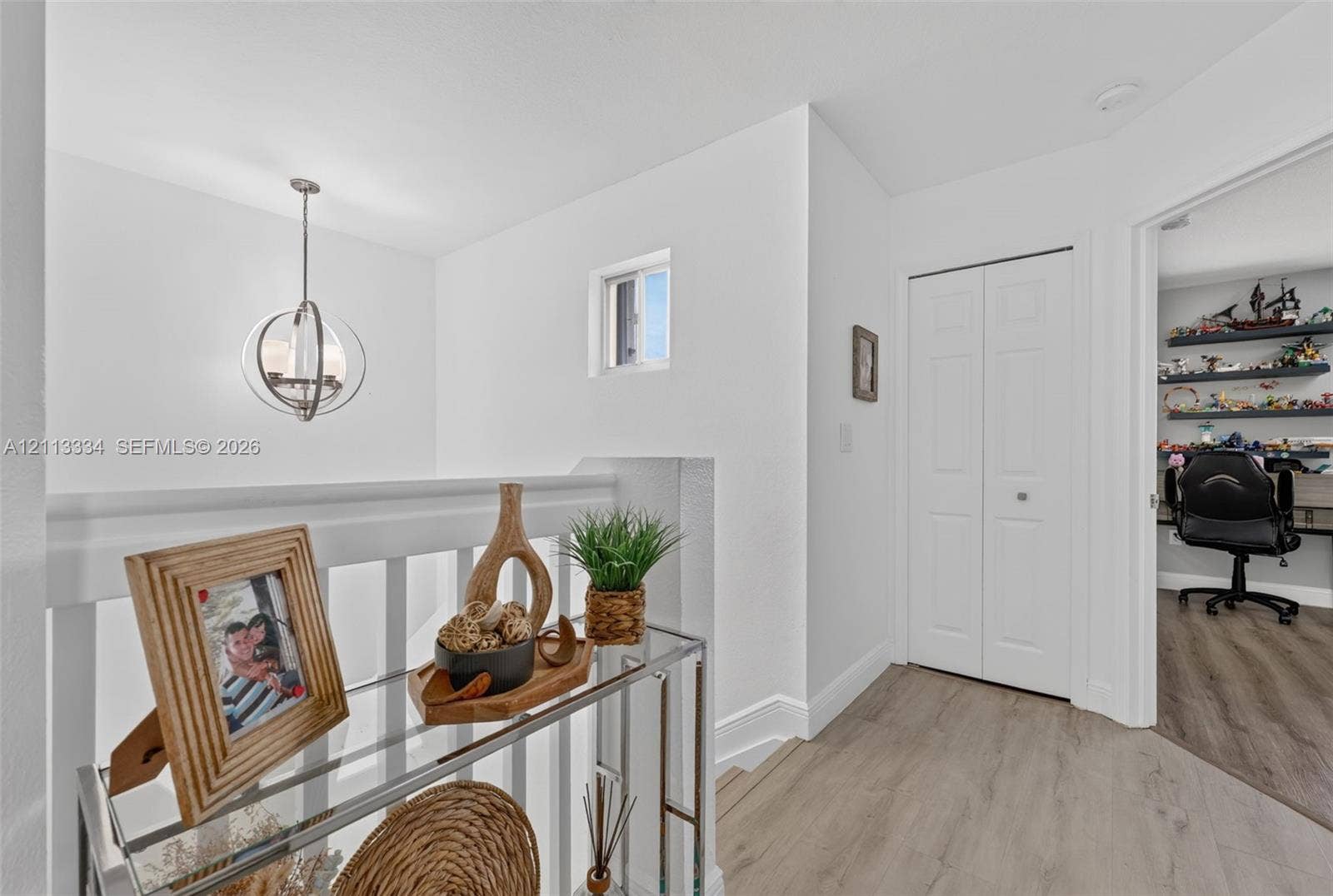28232 SW 128th Path, Homestead, FL 33033 Hallway featuring wood-finish flooring, a contemporary spherical pendant light, a white bifold closet door, and a white baluster railing