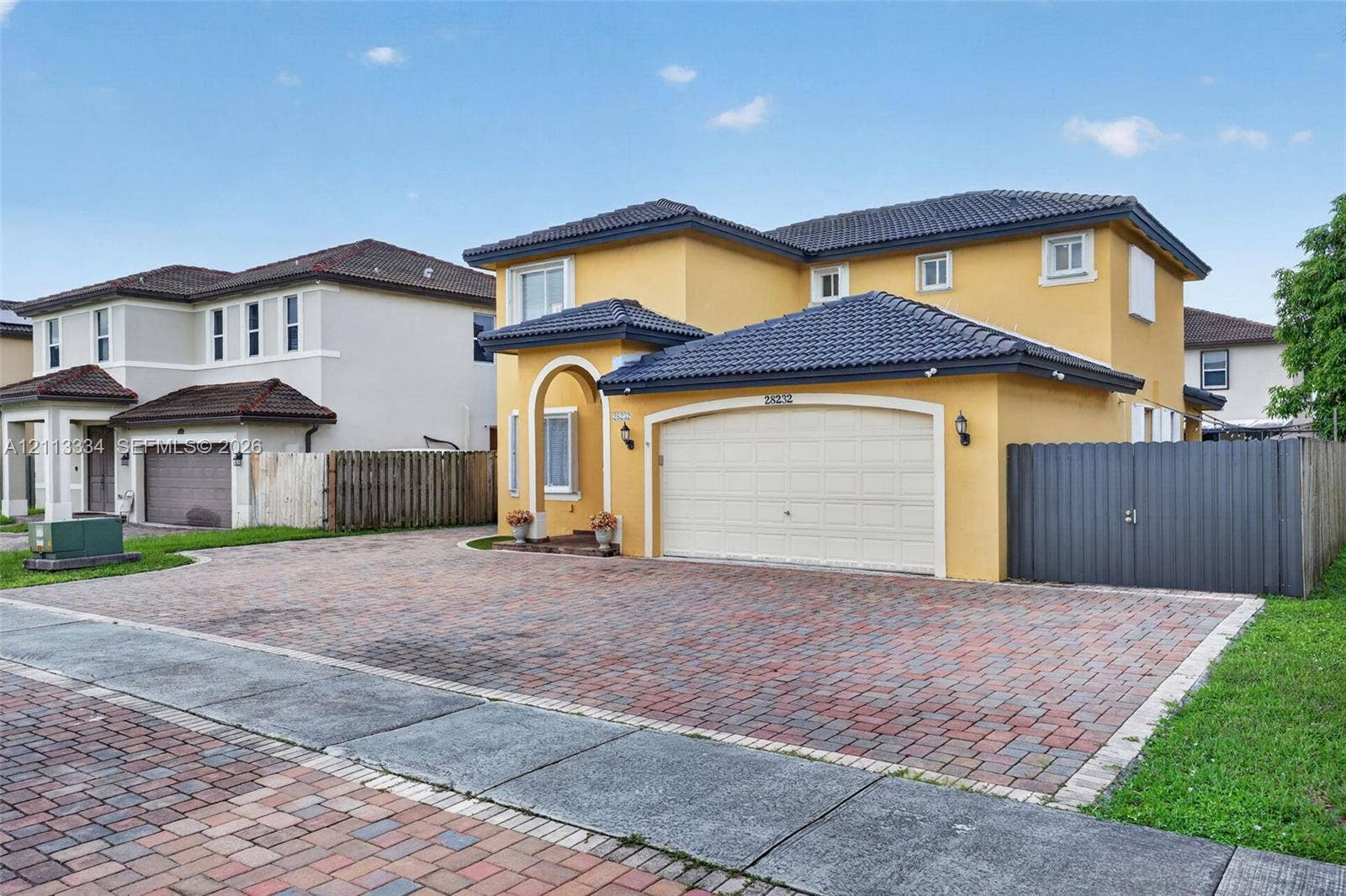 28232 SW 128th Path, Homestead, FL 33033 Two-story exterior featuring a stucco facade, tiled roof, arched entryway, and a multi-car brick paver driveway