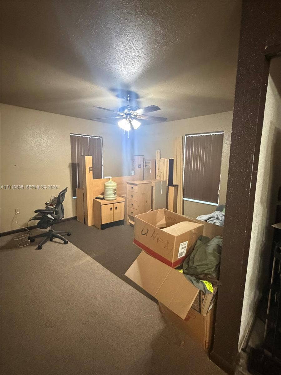 1990 NW 1st Place, Miami, FL 33136 Room featuring neutral-toned carpeting, two windows with vertical blinds, and a ceiling-mounted fan with integrated light fixture