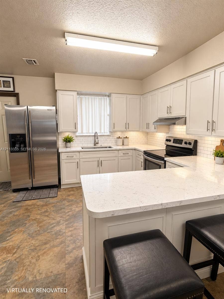 1990 NW 1st Place, Miami, FL 33136 Kitchen featuring white shaker-style cabinetry, quartz countertops, subway tile backsplash, stainless steel refrigerator, and range with integrated hood
