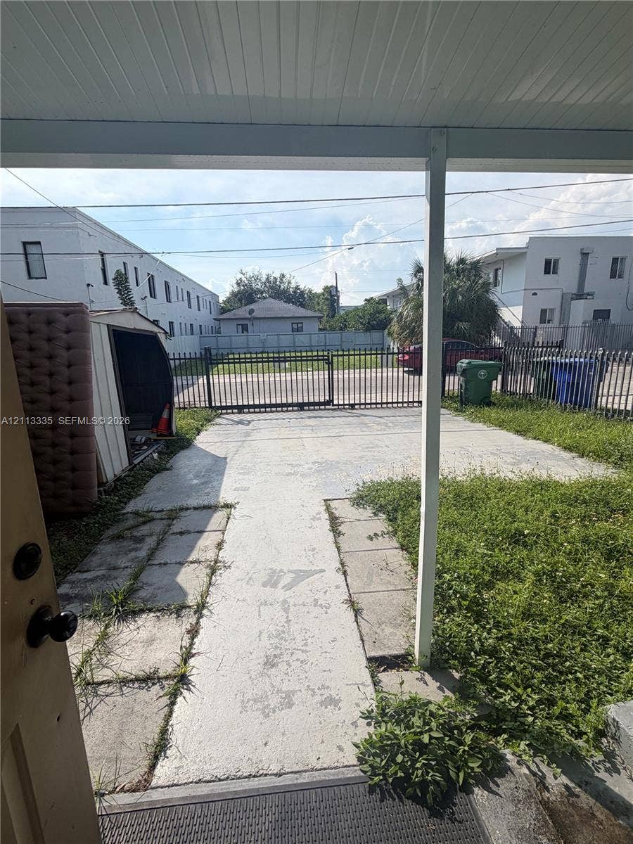 1990 NW 1st Place, Miami, FL 33136 Covered porch entry featuring a concrete parking pad, metal security fencing, and gated access