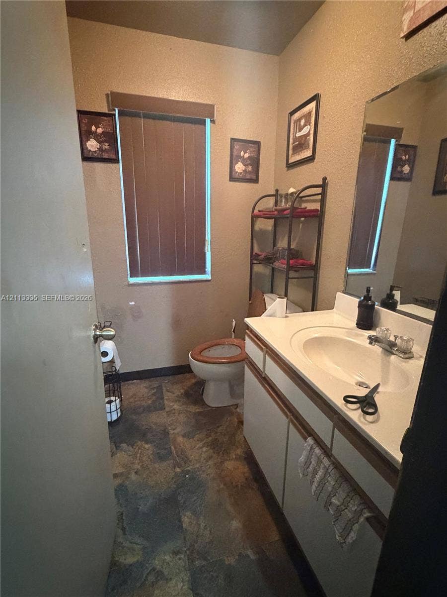 1990 NW 1st Place, Miami, FL 33136 Bathroom featuring a vanity with an integrated sink, neutral-toned cabinetry, a large wall-mounted mirror, and stone-finish flooring