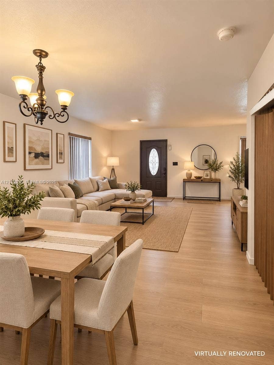 1990 NW 1st Place, Miami, FL 33136 Open-concept interior featuring light wood-finish flooring, a decorative chandelier with classic scrolled arms, and a dark-toned exterior entry door with an oval glass insert