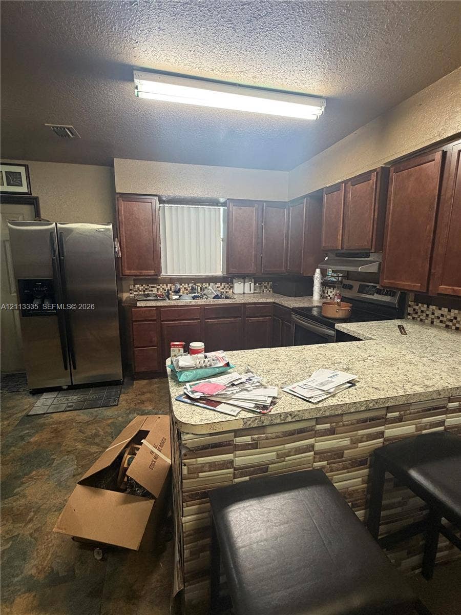 1990 NW 1st Place, Miami, FL 33136 Kitchen featuring dark-toned wooden cabinetry, stone-finish countertops, stainless steel appliances, a tiled backsplash, and stone-finish flooring