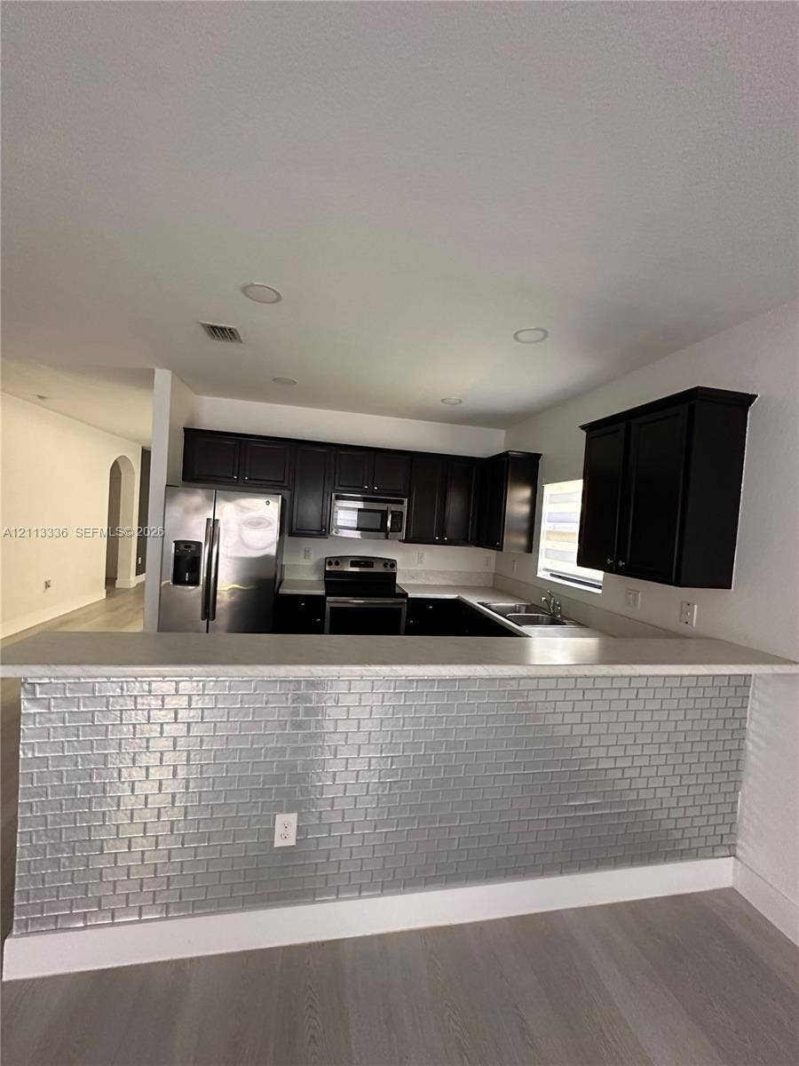 Kitchen featuring dark cabinetry, stainless steel appliances, a metallic brick-patterned breakfast bar, and recessed ceiling lighting