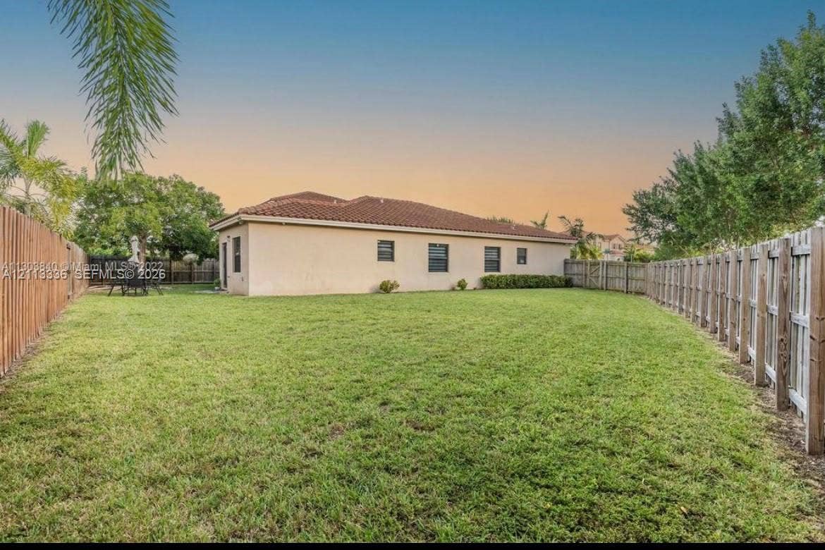 Private rear grounds featuring a sprawling lawn, wood perimeter fencing, and a stucco exterior with a tile roof