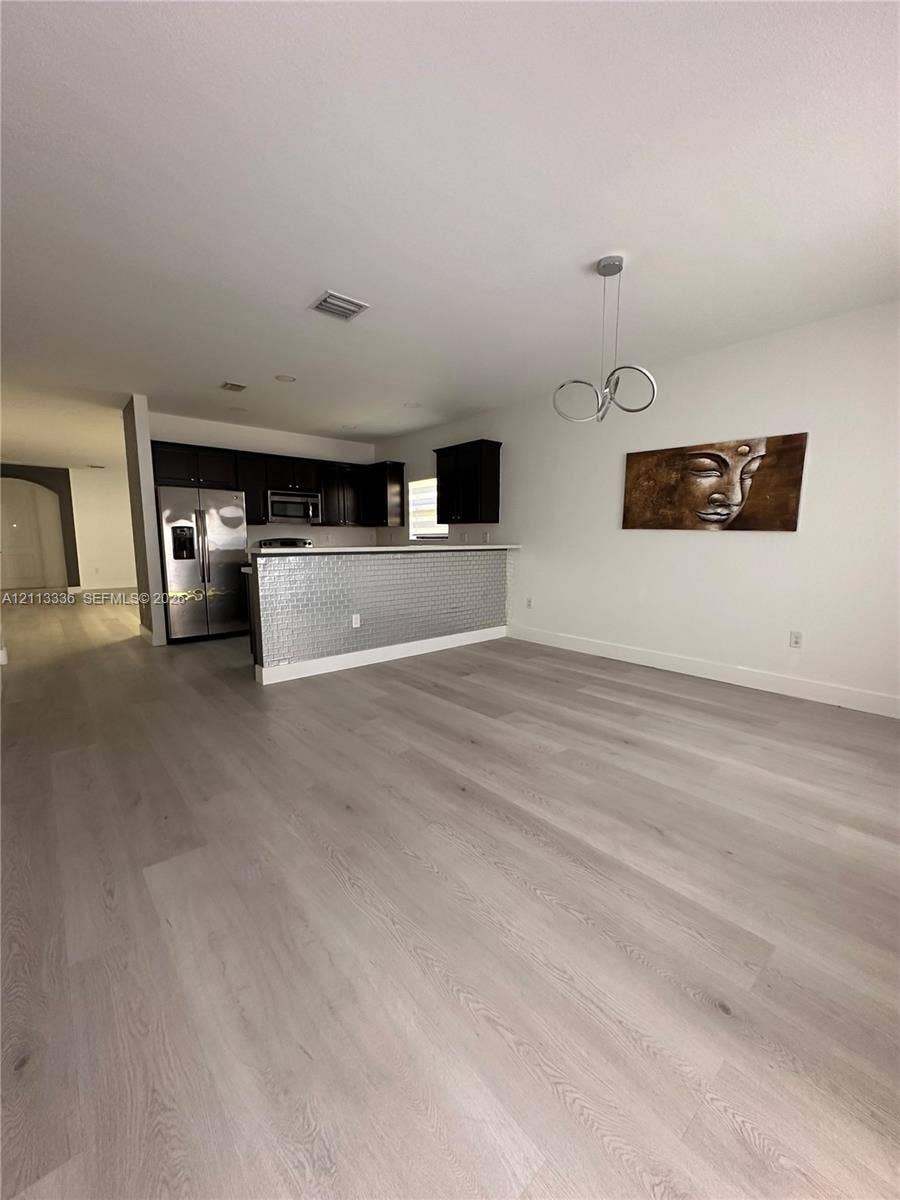 Kitchen area featuring dark cabinetry, stainless steel appliances, a metallic textured breakfast bar, and wood-finish flooring