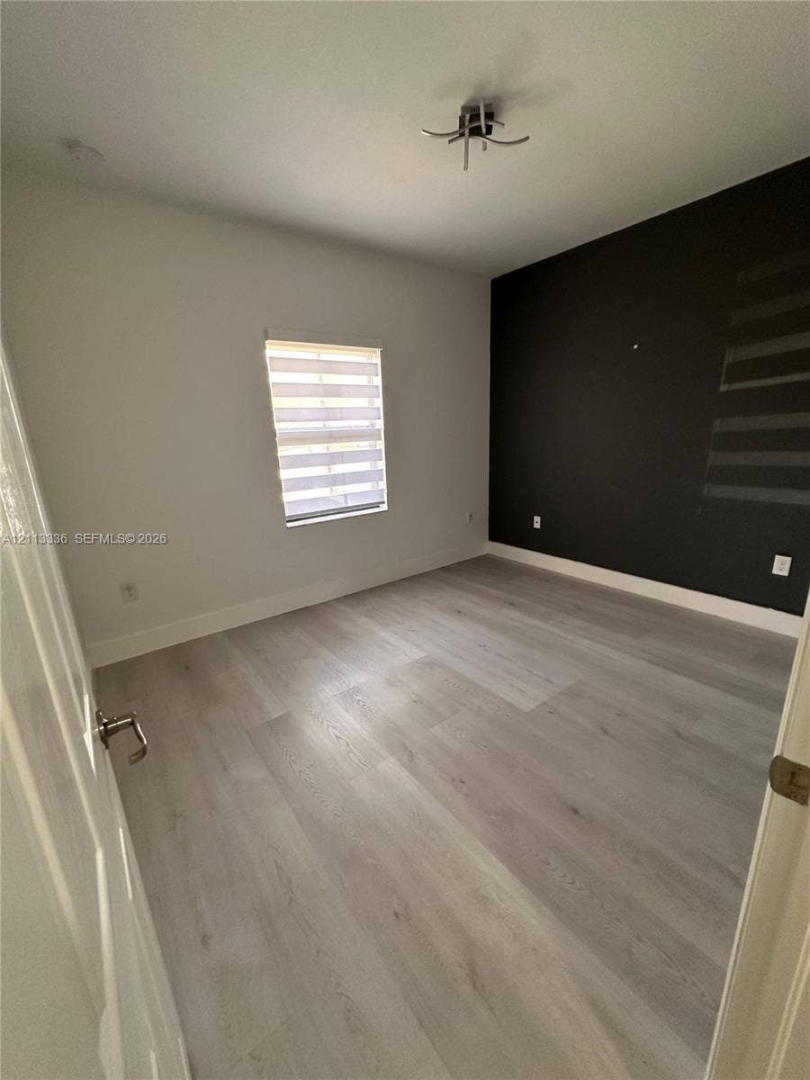 Interior room featuring wood-finish flooring, a charcoal accent wall, and a window with zebra-style light-filtering shades