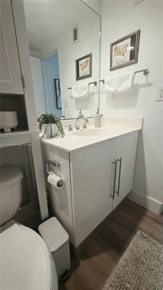 3001 S Ocean Drive, #1539, Hollywood, Hollywood, FL 33019 Vanity featuring a white cabinetry base, integrated sink, countertop, and polished hardware, complemented by a floor-to-ceiling mirror and wood-finish flooring