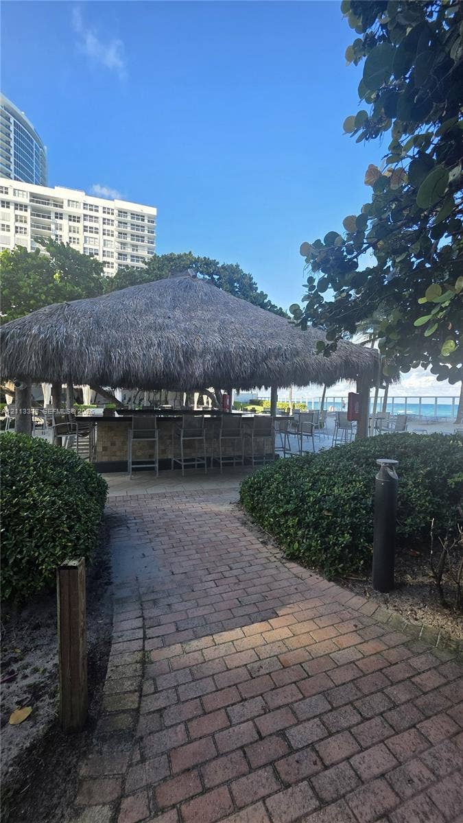 3001 S Ocean Drive, #1539, Hollywood, Hollywood, FL 33019 Outdoor tiki bar with a thatched roof, stone-finish base, and brick-paver walkway surrounded by manicured shrubbery