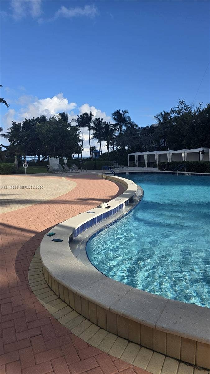 3001 S Ocean Drive, #1539, Hollywood, Hollywood, FL 33019 Curved swimming pool featuring a concrete coping, tile border, patterned paver deck, and multiple cabanas