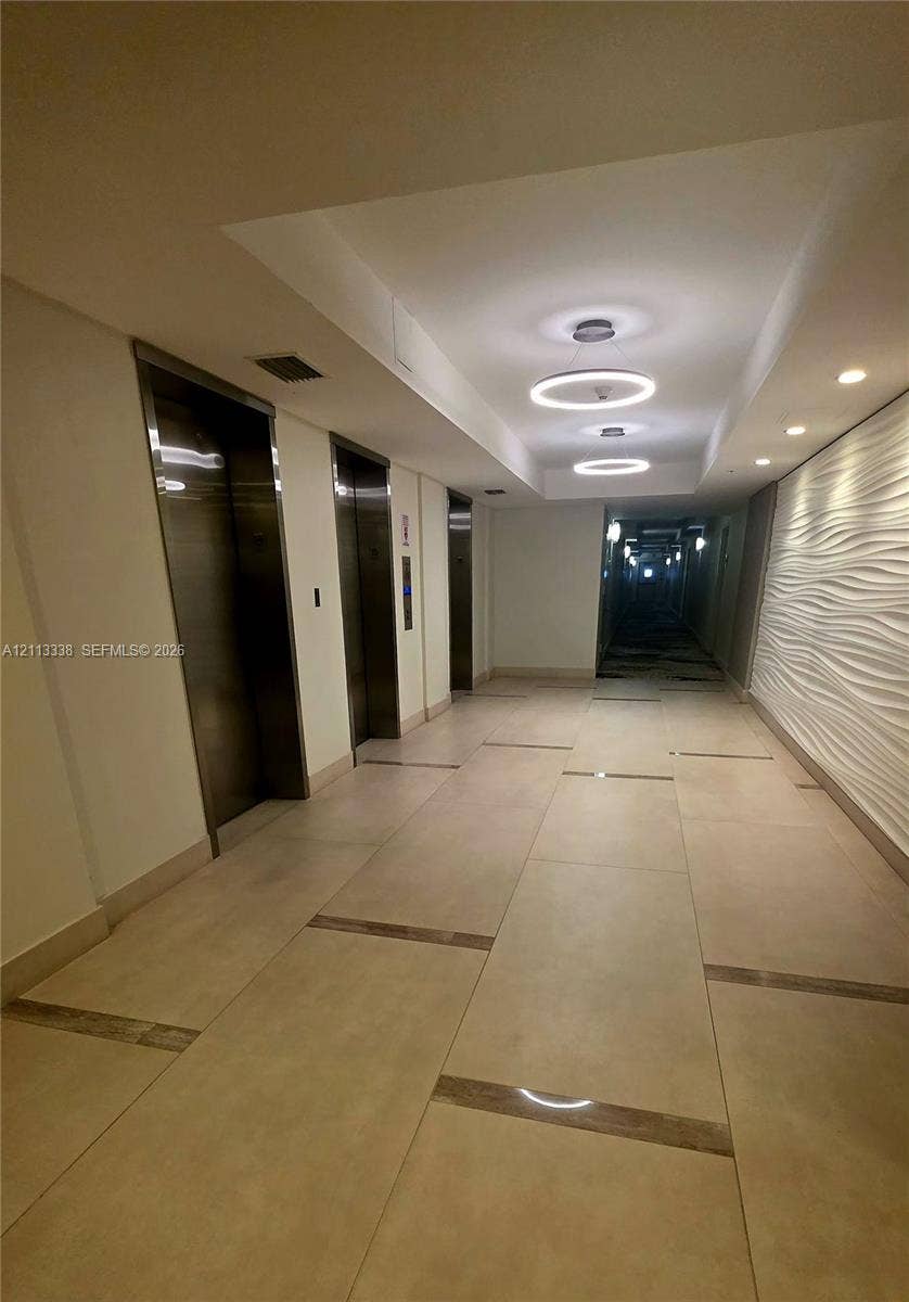 3001 S Ocean Drive, #1539, Hollywood, Hollywood, FL 33019 Elevator lobby featuring metallic-finish doors, large-format tile flooring with inlaid stone accents, textured three-dimensional wall paneling, and circular LED pendant lighting