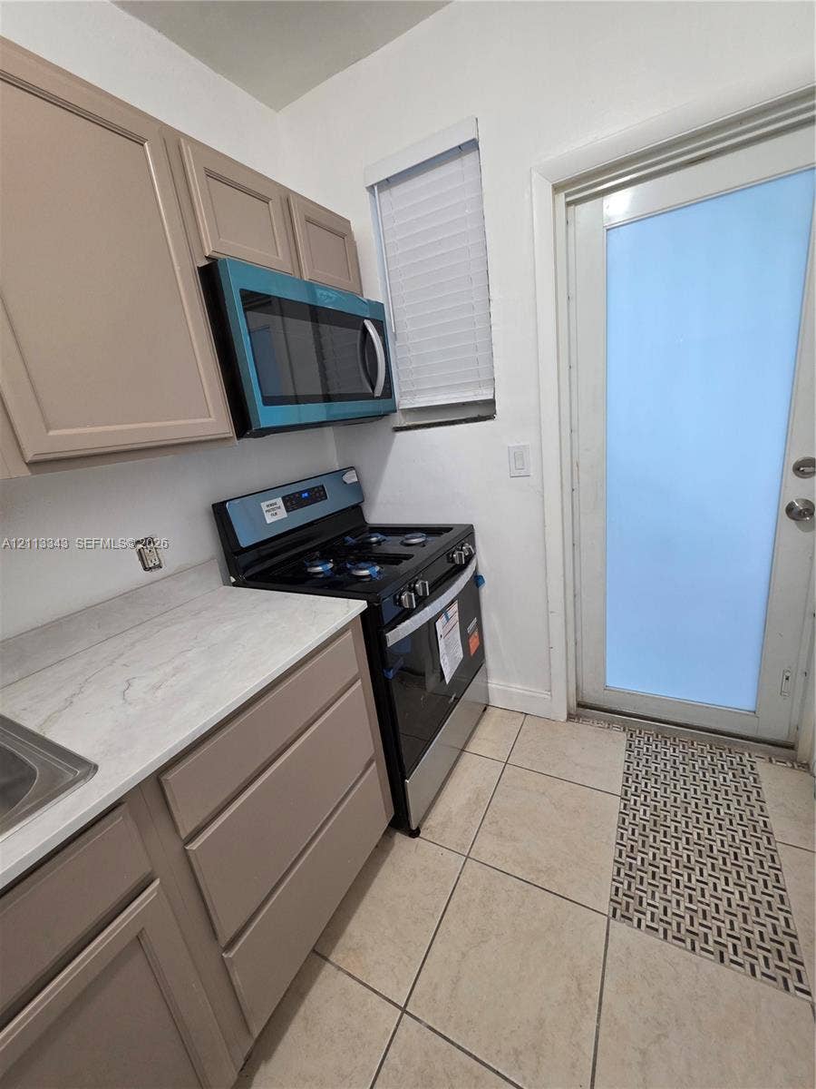 7207 Bay Drive, #2, Miami Beach, Miami Beach, FL 33141 Kitchen area featuring light-toned cabinetry, solid surface countertops, a full-size range, an integrated over-the-range microwave, and ceramic tile flooring