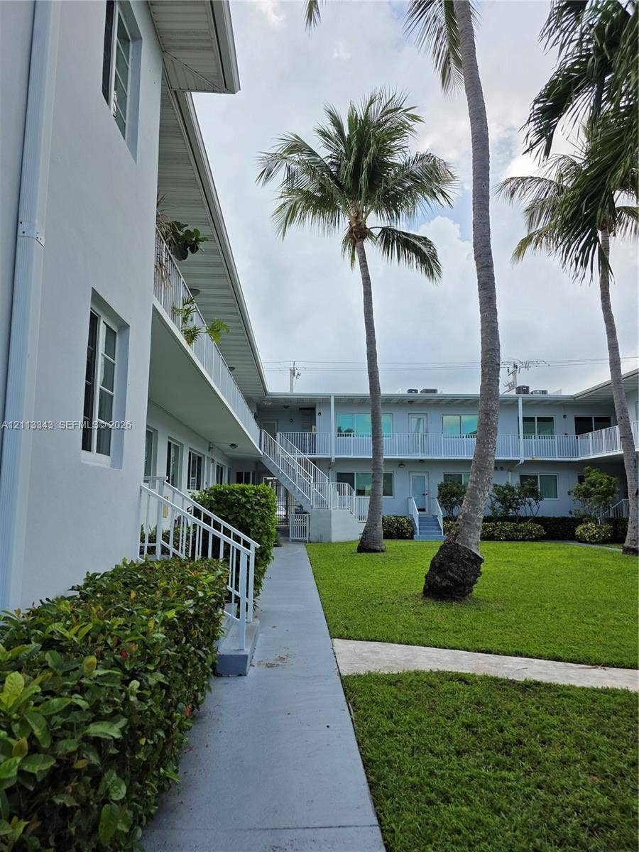 7207 Bay Drive, #2, Miami Beach, Miami Beach, FL 33141 Multi-story exterior featuring light-colored stucco siding, metal staircases with white railings, manicured green space, and mature palm trees