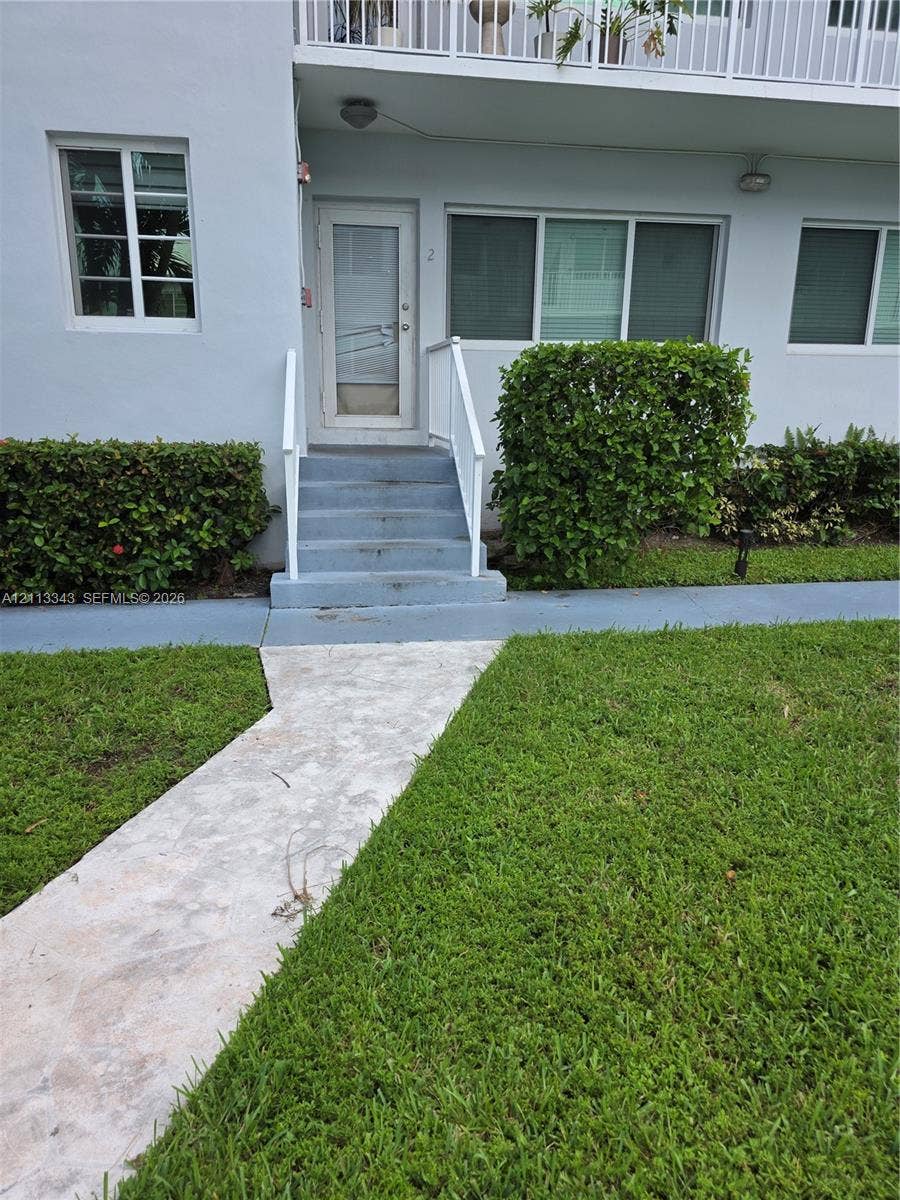 7207 Bay Drive, #2, Miami Beach, Miami Beach, FL 33141 Exterior entrance featuring concrete stairs with white handrails, a glass-panel door, stone-paver walkway, and manicured hedges