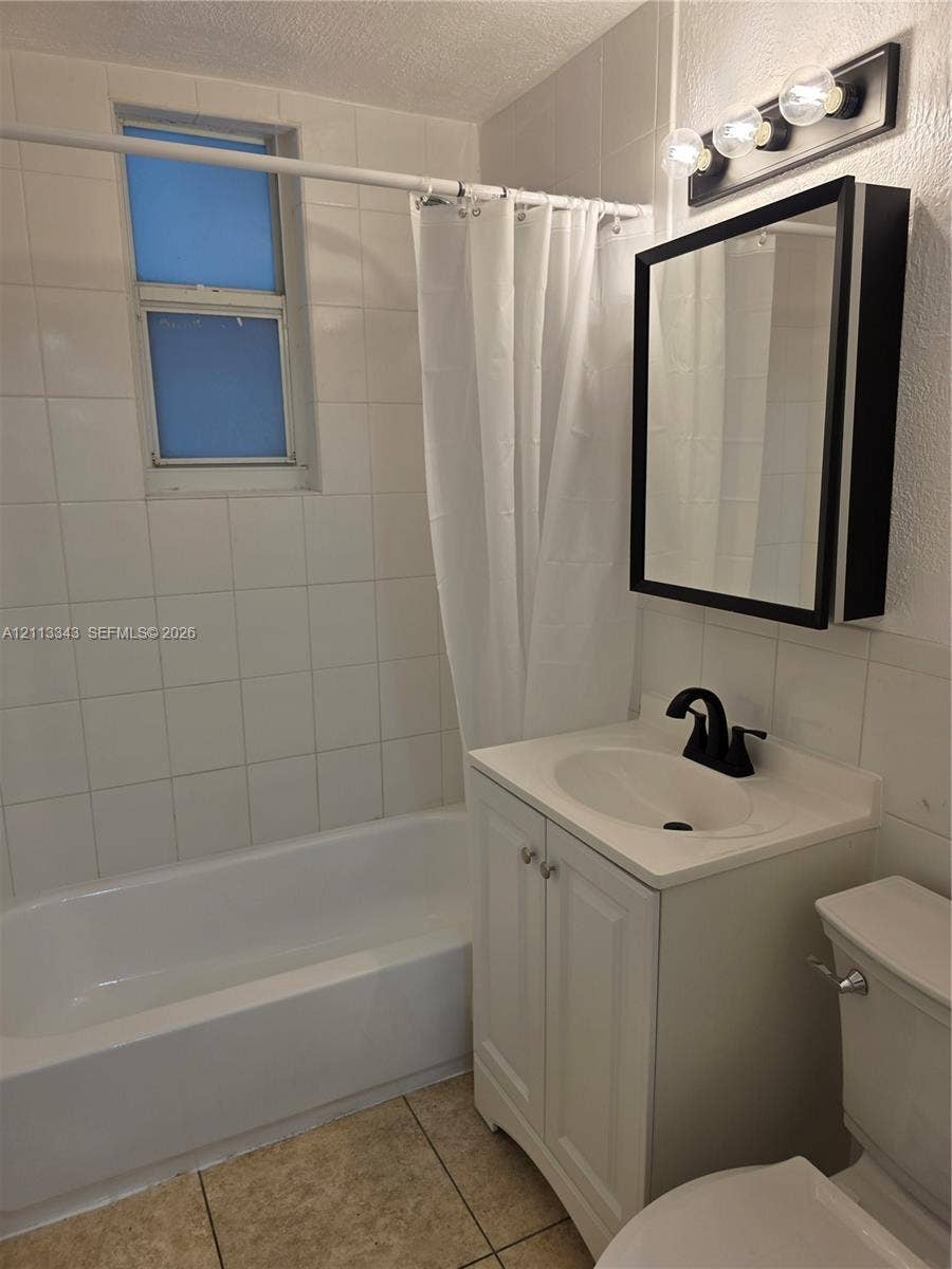 7207 Bay Drive, #2, Miami Beach, Miami Beach, FL 33141 Bathroom featuring white wall-tile surround, vanity with integrated basin, matte black hardware, medicine cabinet, and three-bulb vanity light fixture