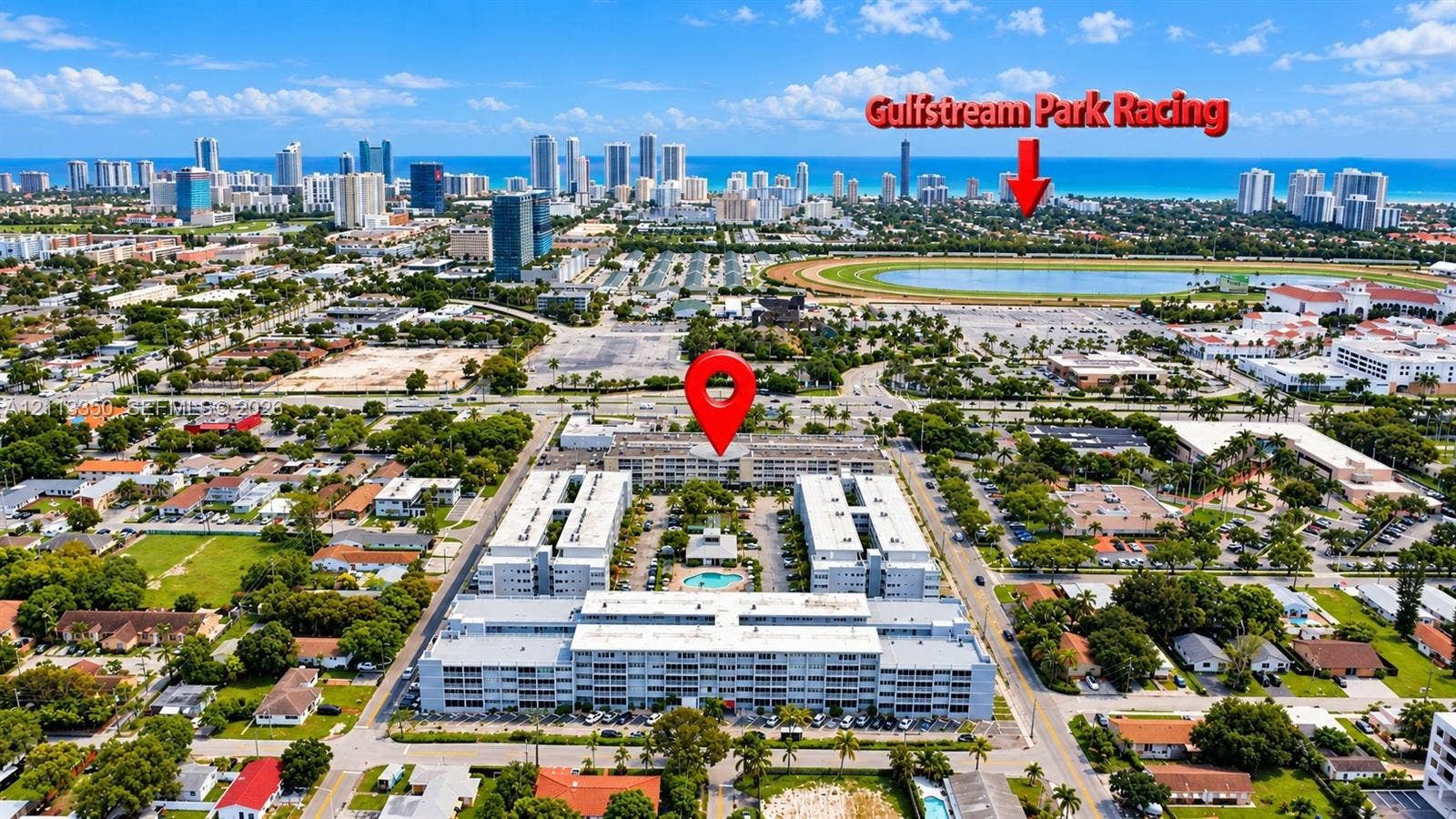 Aerial perspective of a multi-story residential complex featuring a central outdoor swimming pool and perimeter surface parking