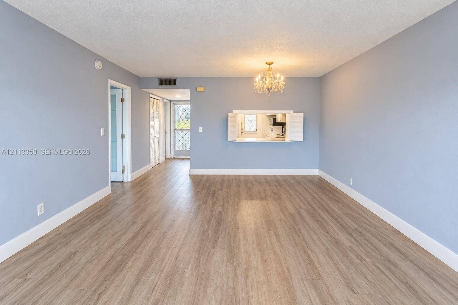 Open-concept room featuring wood-finish flooring, a pass-through window with cabinet doors, a crystal-style chandelier, and glass-paneled entry doors