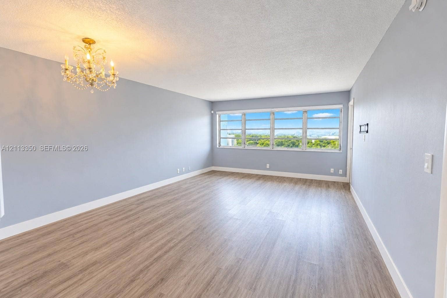Expansive room featuring wood-finish flooring, multi-pane windows, and a decorative chandelier
