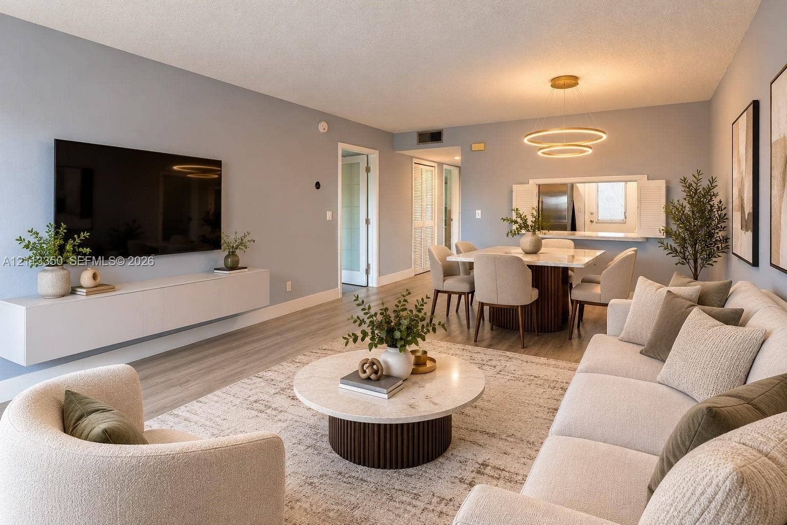 AI RENDERING-Open-concept living space featuring wood-finish flooring, a contemporary dual-ring chandelier, and a wall-mounted floating media console