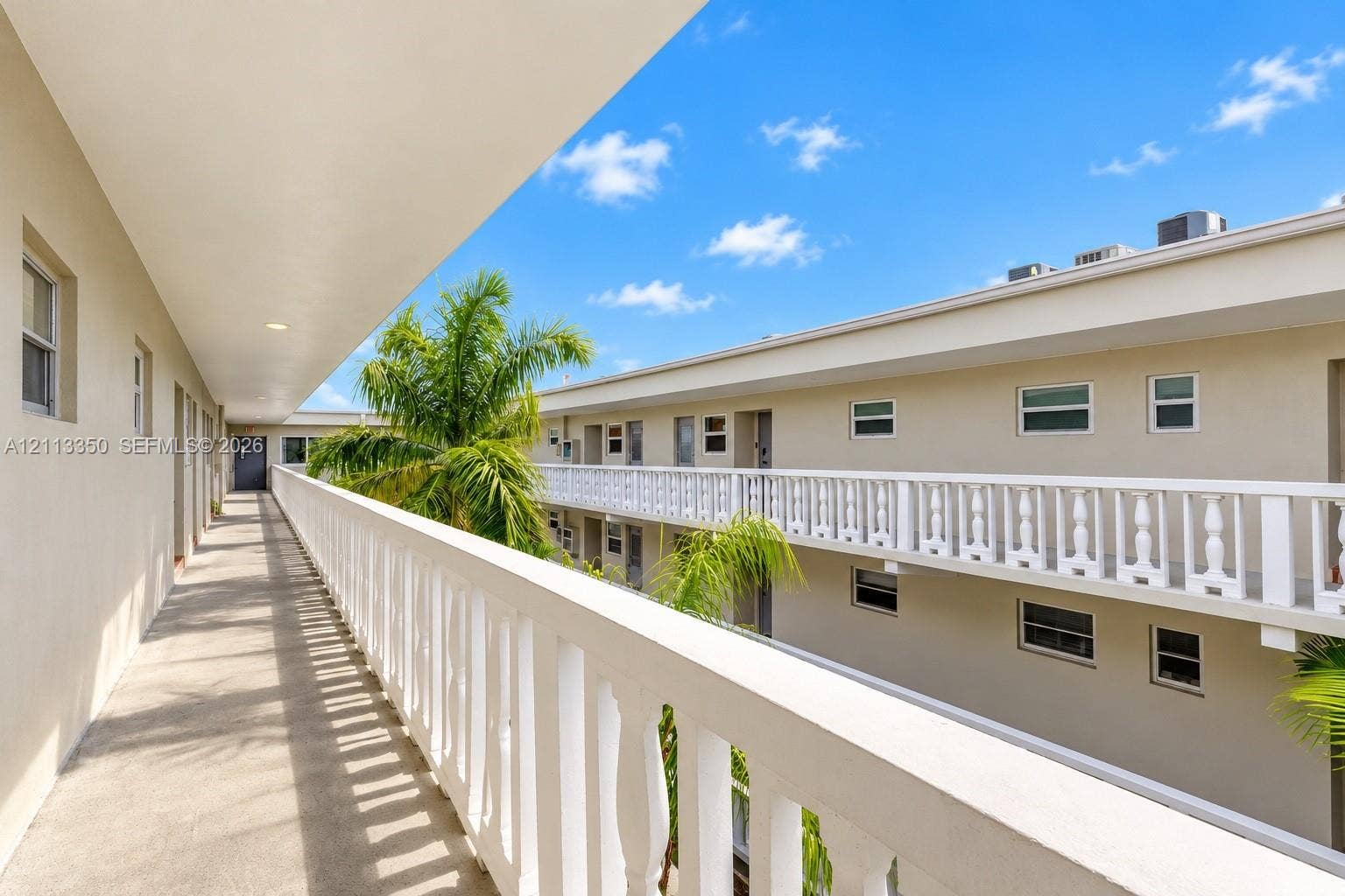 Exterior walkway featuring a concrete floor, white balustrade railings, and mature palm trees