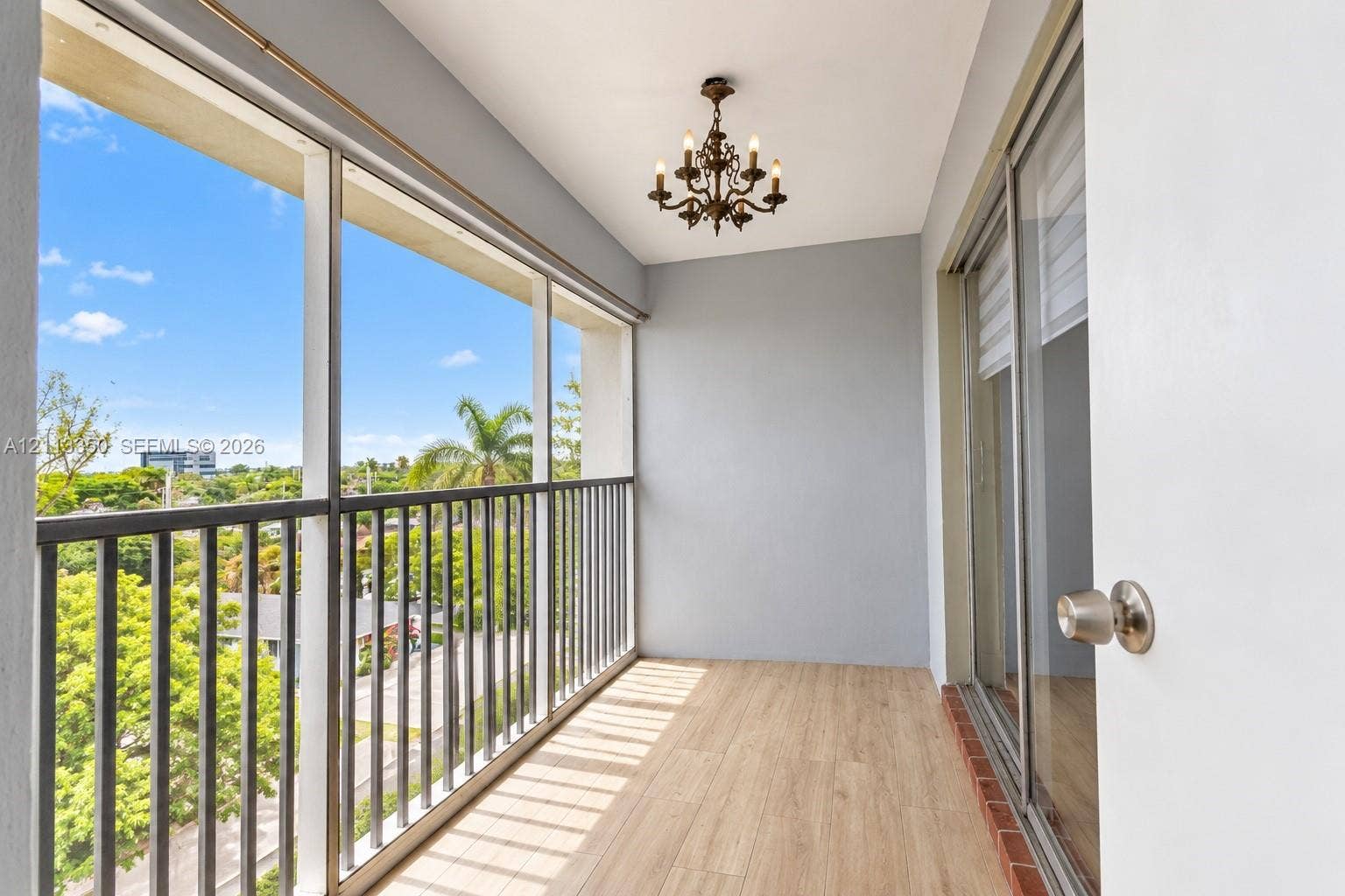 Covered balcony featuring wood-finish flooring, a metal railing, and a decorative candelabra-style light fixture
