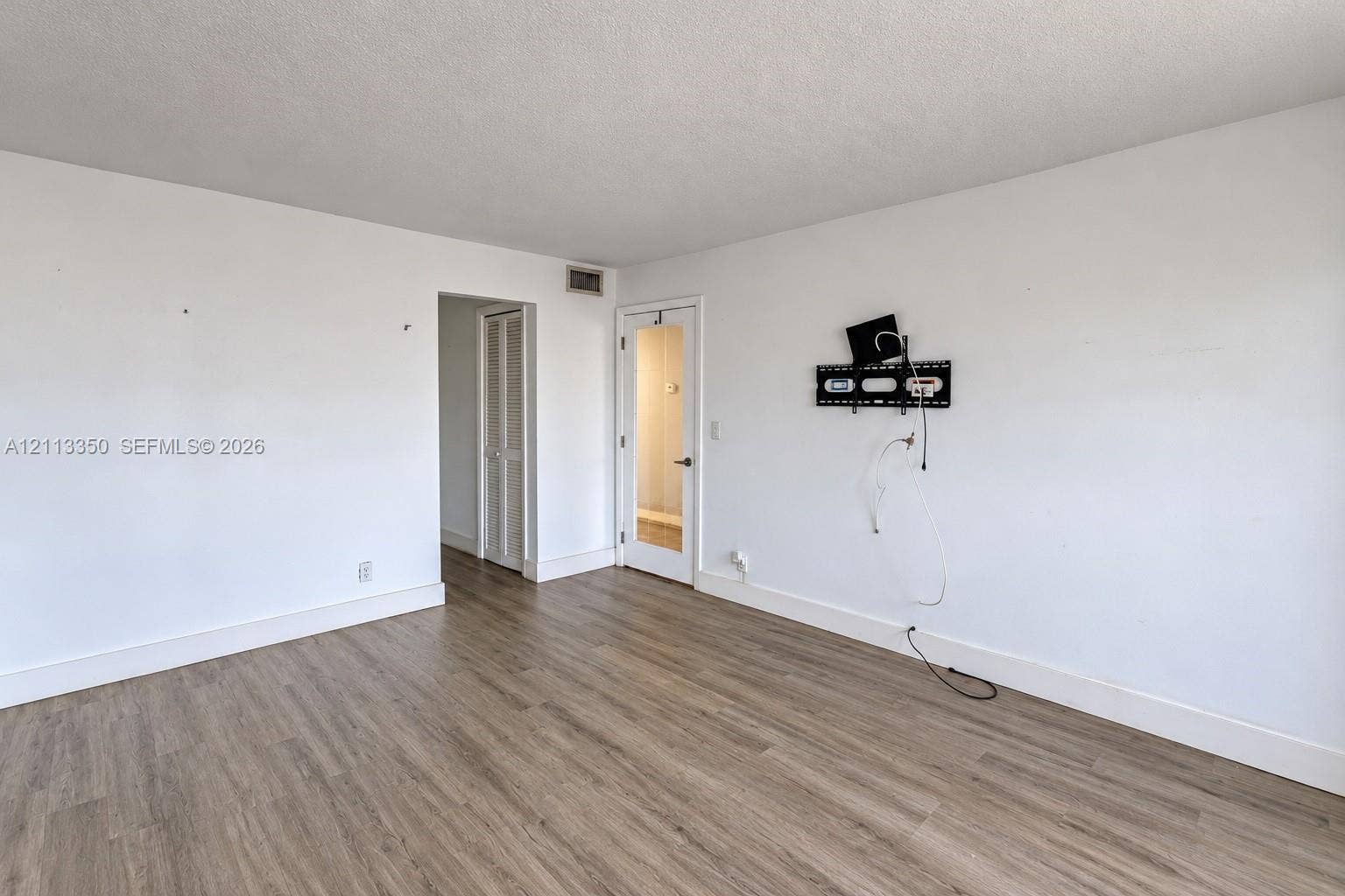 Wood-finish flooring, white walls, louvered closet door, and a glass-paneled door