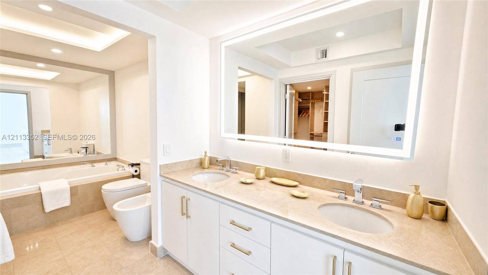 Dual-vanity cabinet with stone-finish countertops, undermount sinks, wall-to-wall LED-backlit mirror, built-in soaking tub, and tile flooring