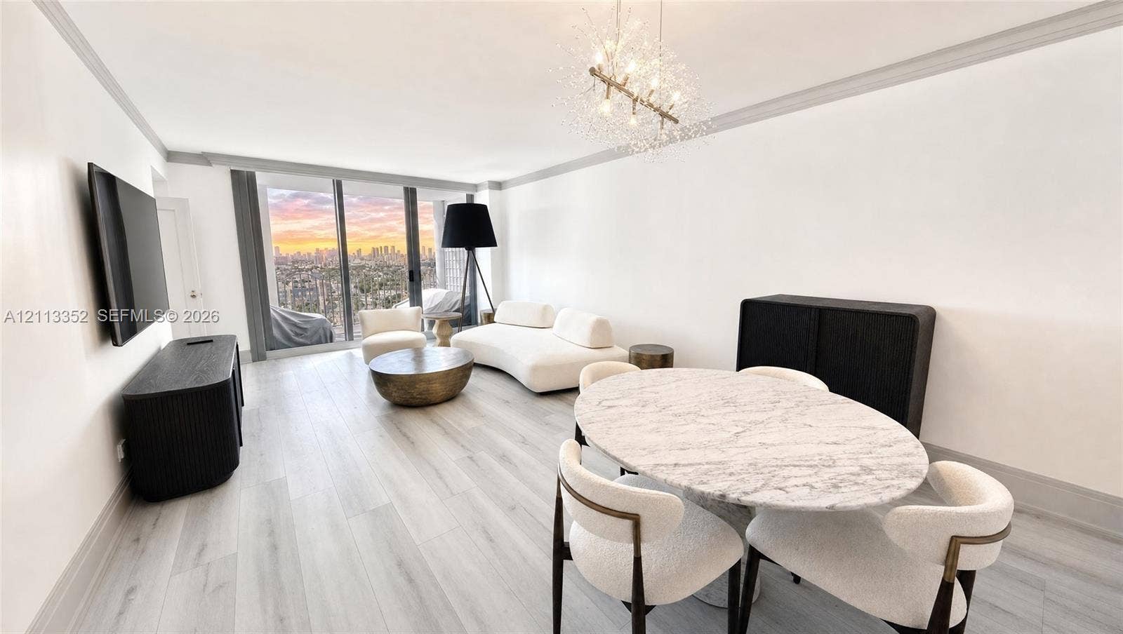 Open-concept living space featuring wood-finish flooring, floor-to-ceiling windows, a metallic starburst chandelier, crown molding, and an expansive cityscape backdrop