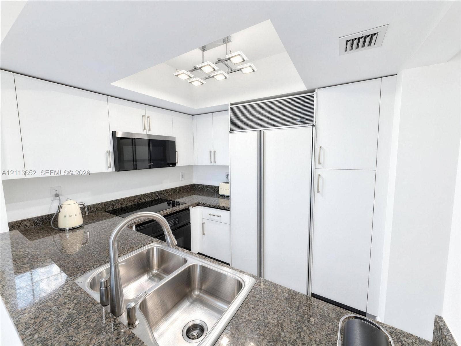 Kitchen featuring white flat-panel cabinetry, stone countertops, stainless steel dual-basin undermount sink, built-in panel-ready refrigerator, and integrated cooktop