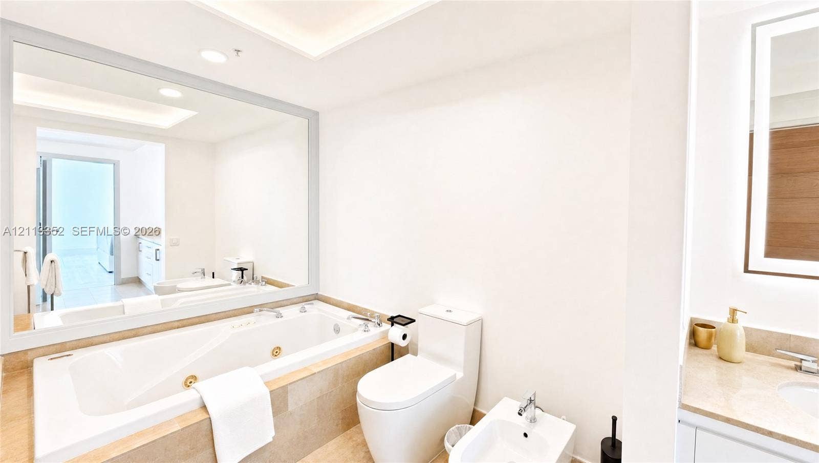 Jetted soaking tub with stone-tiled surround, expansive wall-mounted mirror, dual-piece commode, and bidet