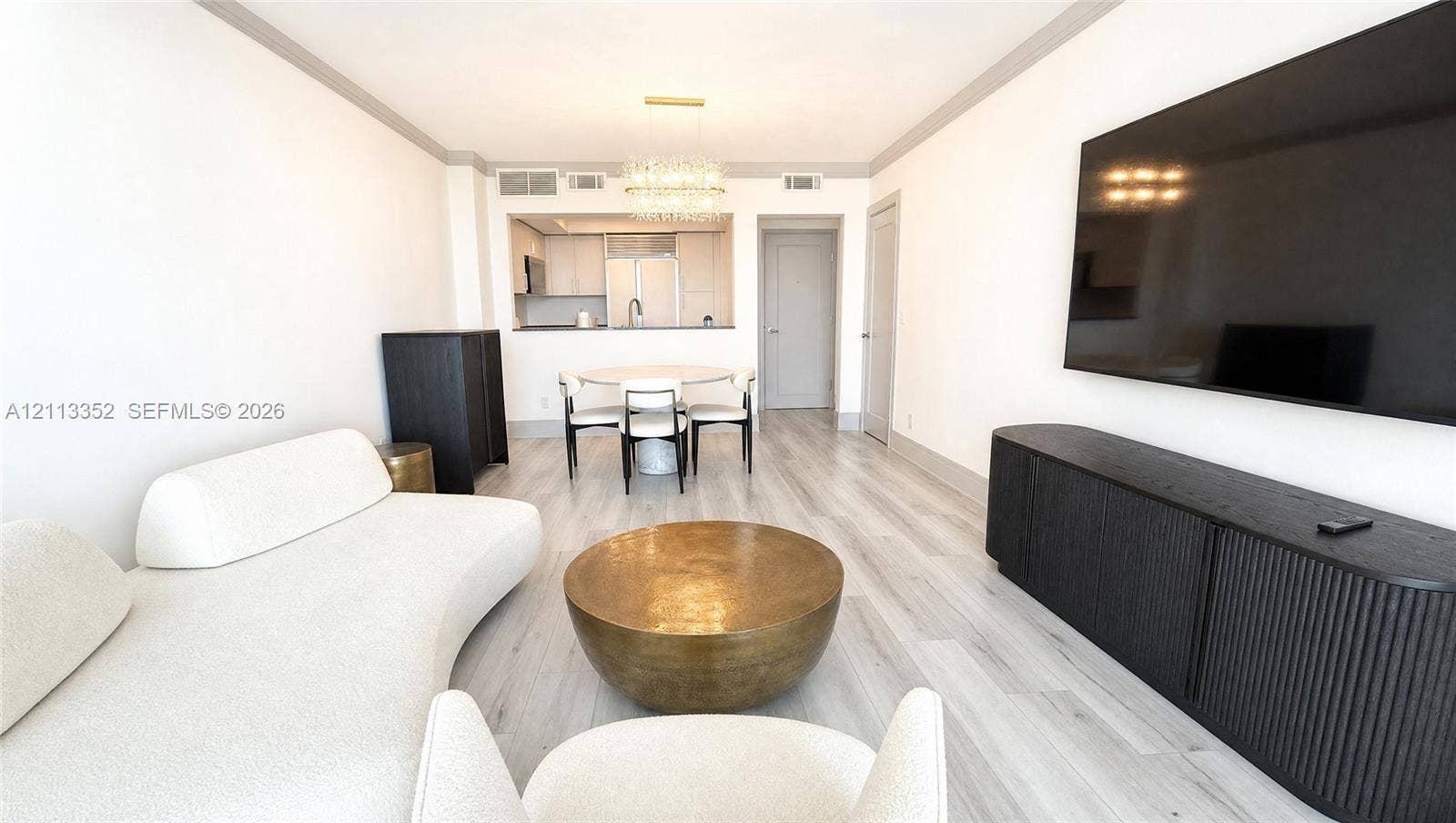 Living space featuring wood-finish flooring, crown molding, and a crystal chandelier