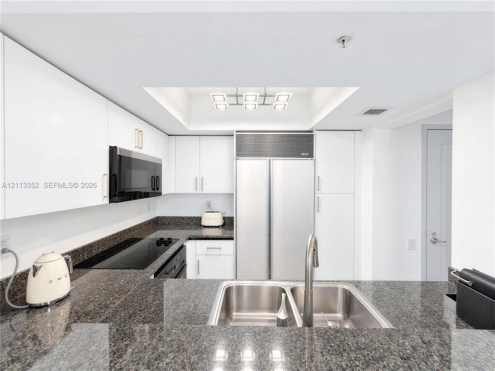Kitchen featuring white flat-panel cabinetry, stone countertops, stainless steel side-by-side refrigerator, built-in microwave, and an undermount double-basin sink