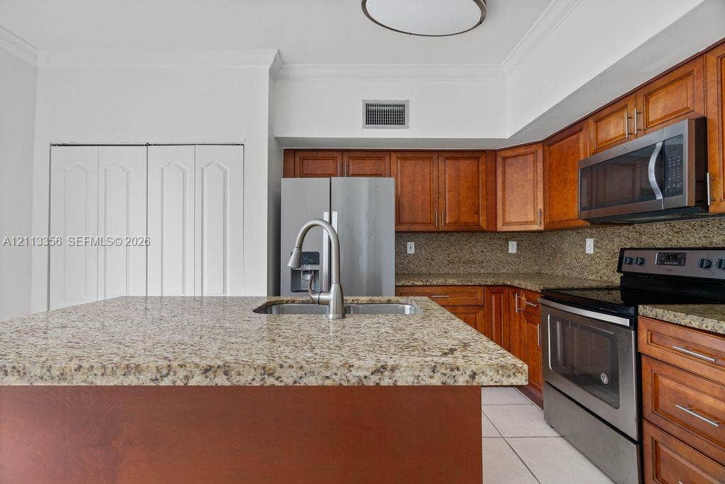 8715 SW 152nd Avenue, #312, Miami, Miami, FL 33193 Kitchen featuring custom wood cabinetry, stone countertops, an island with an integrated stainless steel undermount sink, and stainless steel appliances