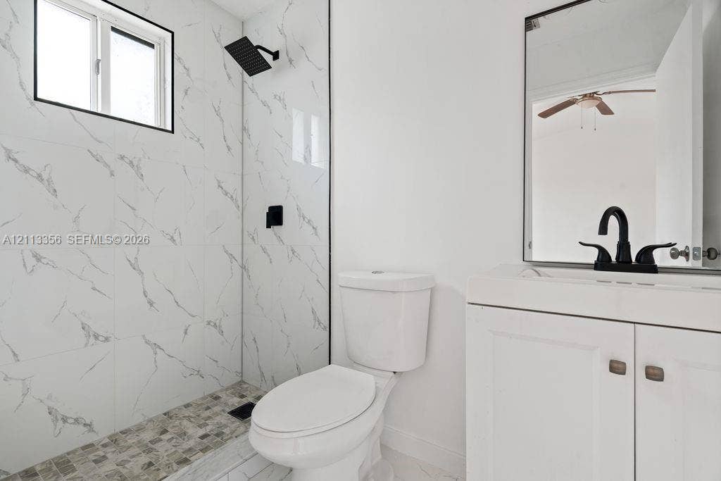 8715 SW 152nd Avenue, #312, Miami, Miami, FL 33193 Bathroom featuring a walk-in shower with stone-patterned tile walls, pebble-style flooring, a matte black rainfall showerhead, a white shaker-style vanity, and a framed mirror