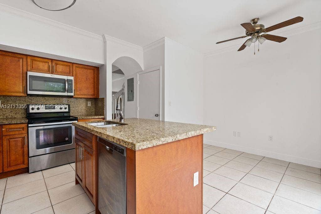 8715 SW 152nd Avenue, #312, Miami, Miami, FL 33193 Kitchen featuring warm-tone wooden cabinetry, stone countertops, stainless steel appliances, a center island with a built-in dishwasher, and ceramic tile flooring