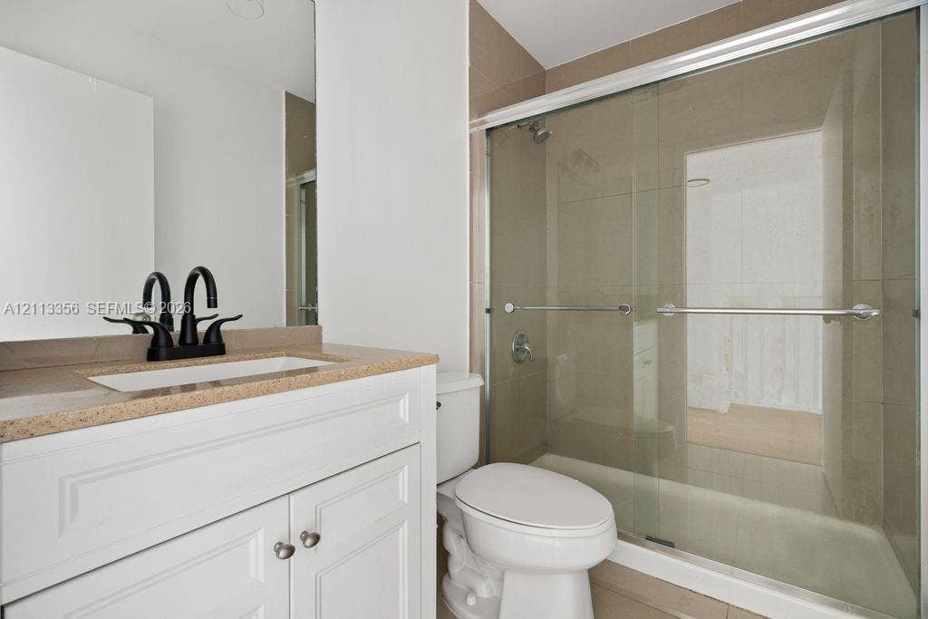 8715 SW 152nd Avenue, #312, Miami, Miami, FL 33193 White vanity cabinet with a stone-finish countertop, integrated rectangular sink, matte black faucet, and a shower enclosure featuring sliding glass doors and neutral tile surround
