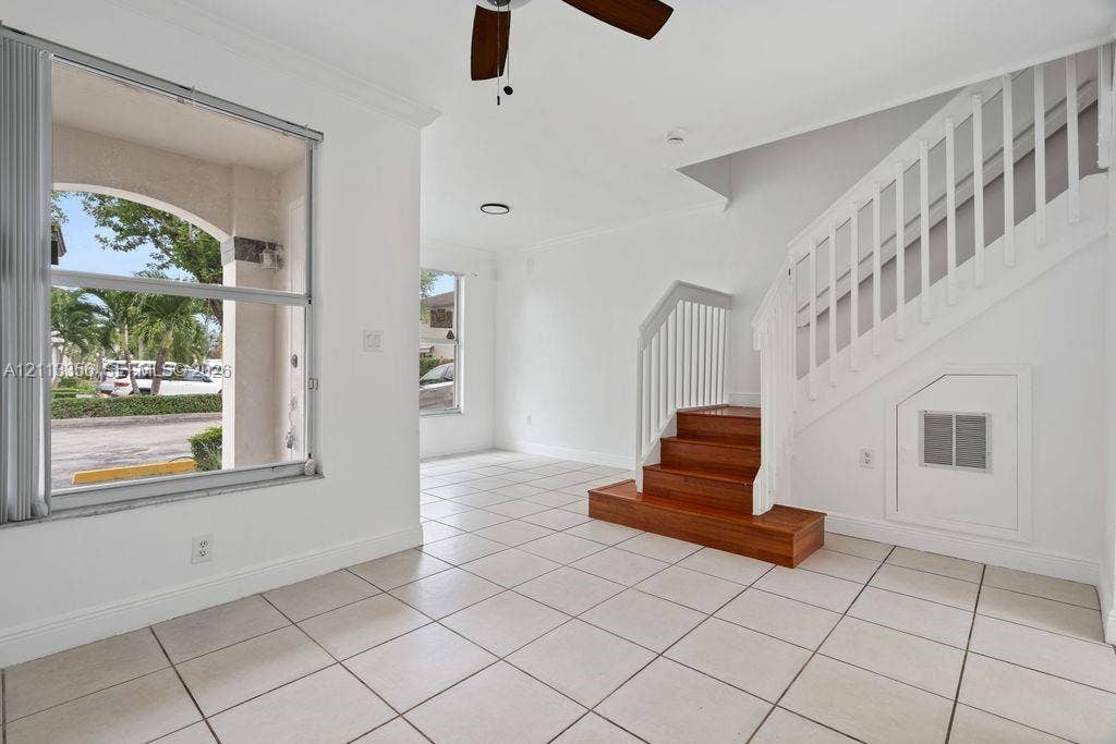 8715 SW 152nd Avenue, #312, Miami, Miami, FL 33193 Open-concept interior featuring light-toned tile flooring, large windows, a ceiling fan, and a staircase with wood-finish treads and white balusters