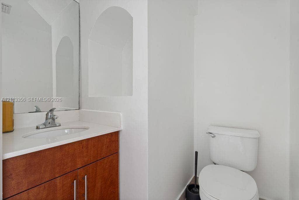 8715 SW 152nd Avenue, #312, Miami, Miami, FL 33193 Wood-finish vanity cabinet, solid-surface countertop with integrated sink, polished chrome faucet, rectangular wall-mounted mirror, and an arched architectural recessed niche