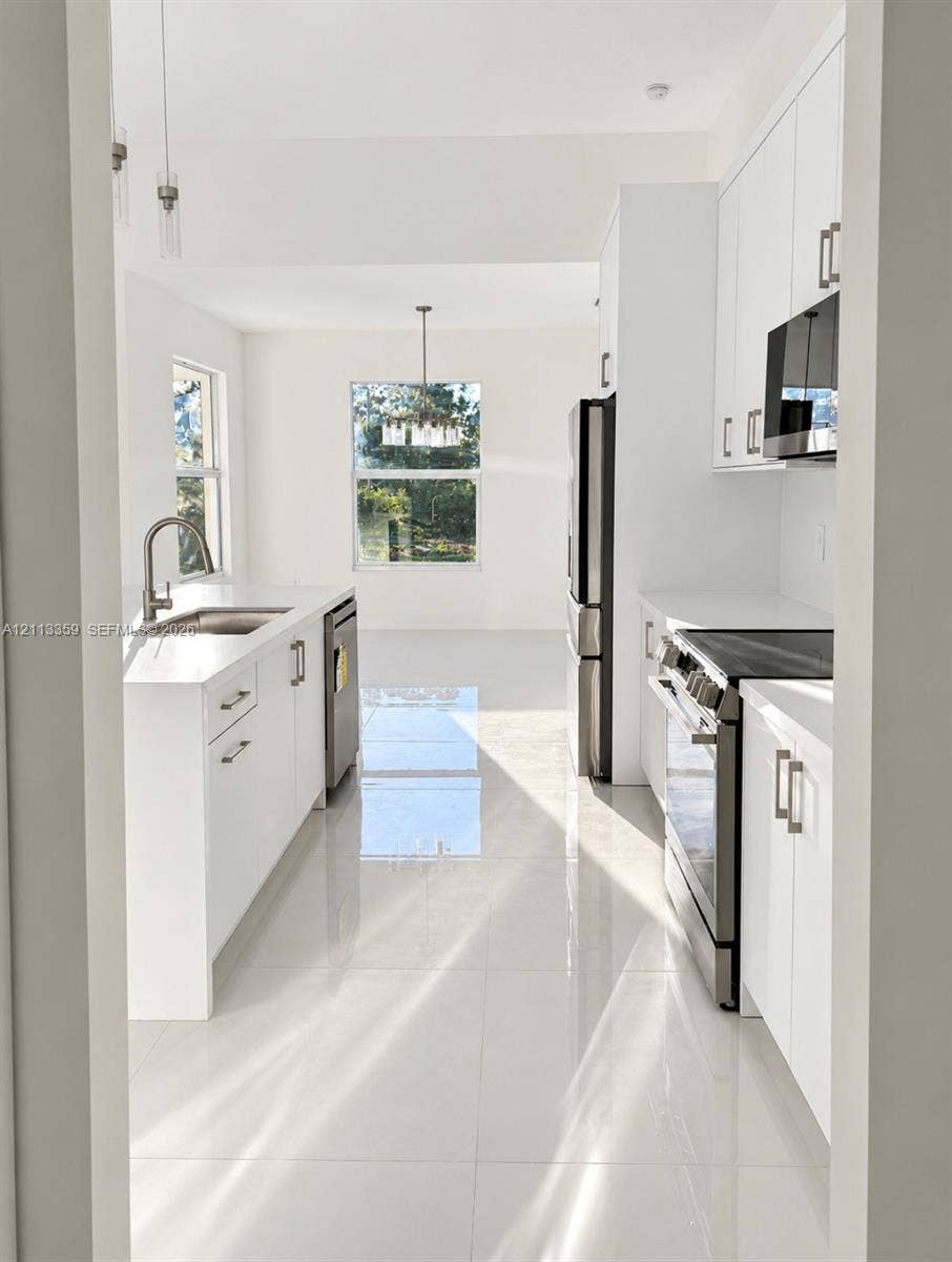 Kitchen featuring white cabinetry, solid-surface countertops, large-format tile flooring, stainless steel appliances, and a polished chrome kitchen faucet
