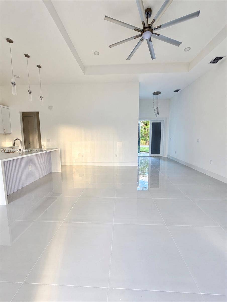 Open-concept interior featuring large-format tile flooring, tray ceilings, recessed lighting, multi-blade ceiling fan, and kitchen peninsula with vertical slat detailing