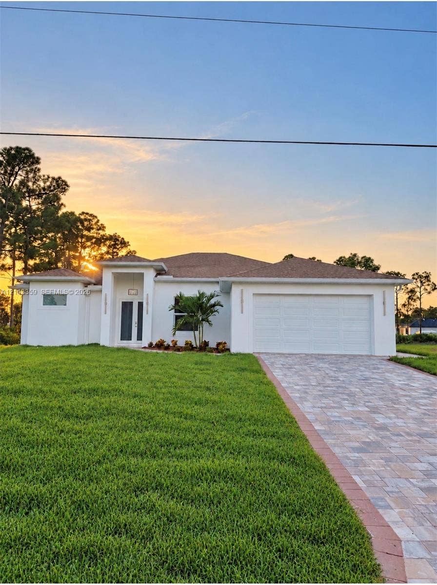 Stucco exterior featuring a multi-hipped roofline, paver driveway, covered entryway, and attached garage