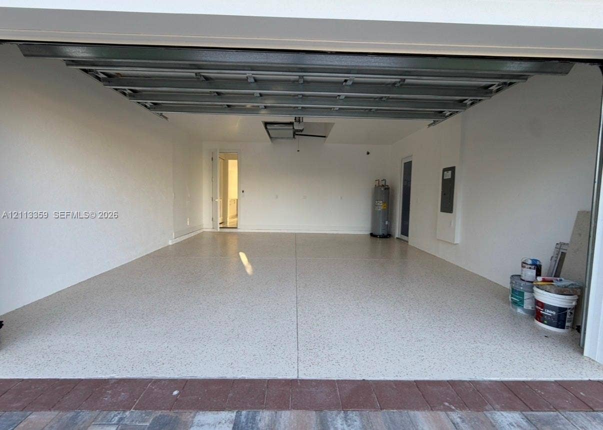 Finished garage featuring epoxy flooring, crisp white walls, exposed steel ceiling joists, an integrated water heater, and a recessed electrical panel
