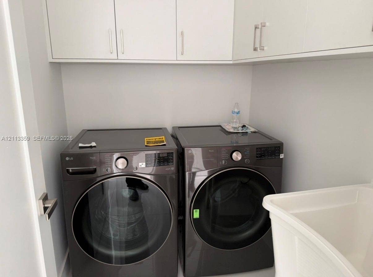 Laundry space featuring charcoal-finish front-load appliances, matte white shaker-style cabinetry with polished metal hardware, and a deep basin utility sink
